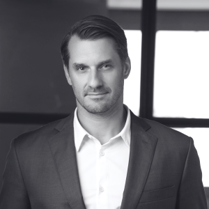 Black and white photo of an individual in a suit jacket and white dress shirt. Professional portrait style, suitable for representing an executive director in private wealth services at Americana Partners.